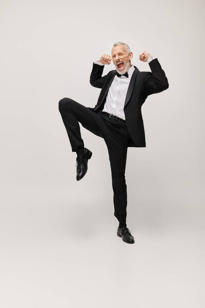 attractive jolly mature man with elegant dapper style with beard dancing happily on gray backdrop