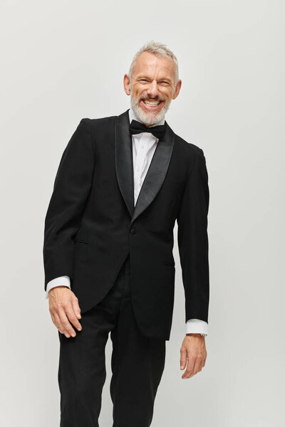 handsome cheerful mature man in black elegant tuxedo with bow tie smiling happily at camera