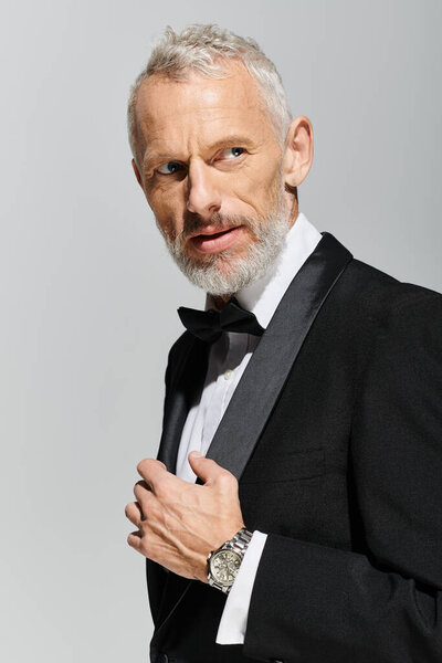 handsome elegant mature man with beard wearing voguish tuxedo with bow tie and looking away