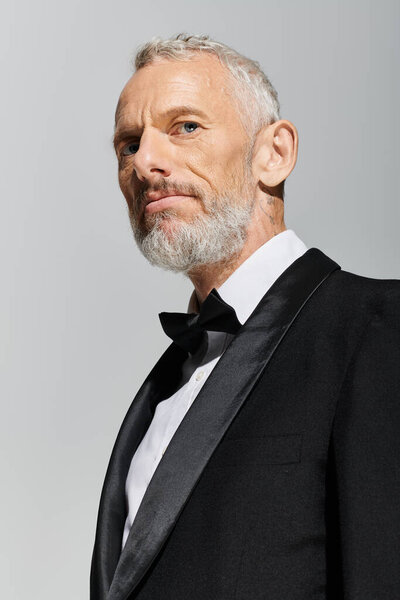 good looking elegant mature man with beard wearing fashionable tuxedo and looking at camera