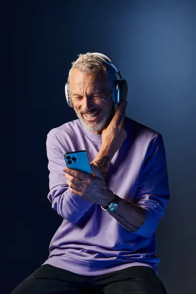 stock image joyful attractive mature man with beard and headphones enjoying music and looking at his phone