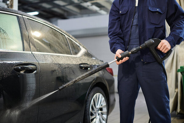 cropped view of devoted serviceman in blue comfy uniform preparing to use hose to wash car in garage