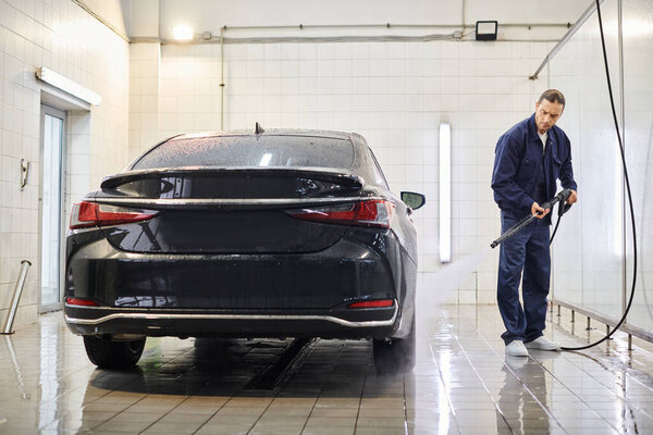 handsome dedicated professional worker with collected hair washing car attentively while in garage