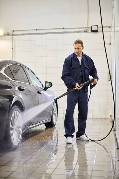 good looking dedicated serviceman in blue uniform with collected hair using hose to wash car