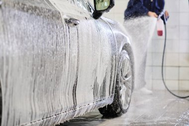 Kendini işine adamış mavi üniformalı bir adamın garajda sabunla araba yıkaması.