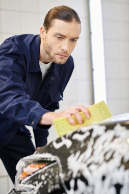 appealing dedicated serviceman with collected hair in blue comfy uniform washing car using sponge clipart