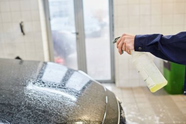 cropped view of enthusiastic professional worker in uniform using pulverizer with water to clean car clipart