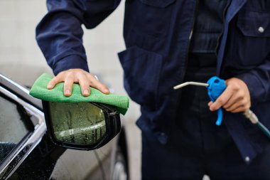 Kendini işine adamış mavi üniformalı bir askerin garajda hortum ve bez kullanarak araba temizlemesi.