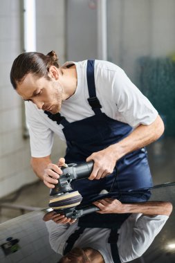 good looking dedicated worker with collected hair in uniform using polishing machine on car clipart