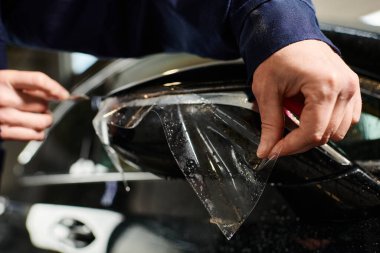 Kesilmiş görüş, siyah araba aynasına yeni koruyucu folyo uygulamak için çok çalışan bir profesyonele adanmıştır.