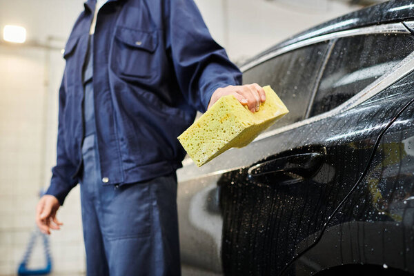 cropped view of dedicated professional serviceman in blue uniform holding sponge next to black car