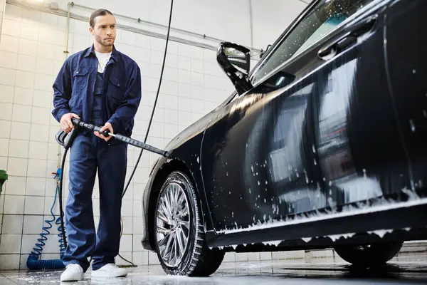 stock image appealing dedicated specialist in blue uniform with collected hair washing car with hose in garage