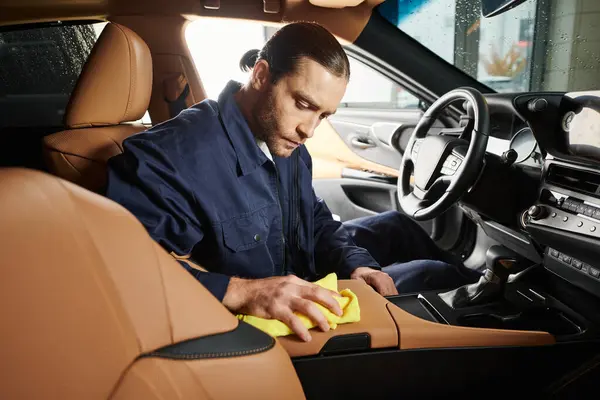 stock image appealing devoted serviceman in blue uniform with collected hair cleaning car with yellow rag