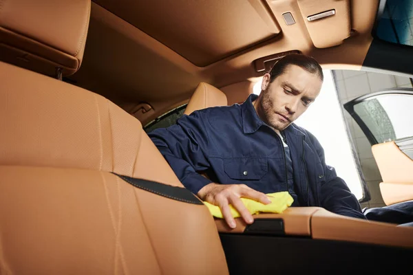 stock image handsome dedicated professional serviceman in uniform with collected hair cleaning car with rag