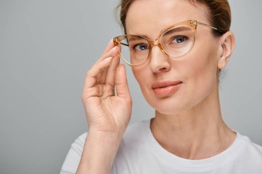 Sarı saçlı, gözlüklü, gri arka planda kameraya gülümseyen çok güzel bir kadın.