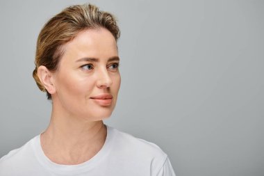 Sarı saçlı, kontak lensli, gri arka planda poz veren ve başka yöne bakan çekici bir kadın model.