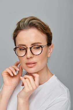 good looking blonde woman with collected hair and glasses posing on gray backdrop and looking away clipart