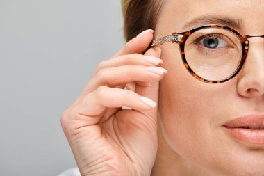 Sarışın ve gözlüklü çekici kadın modelin gri arka planda kameraya baktığı yakın plan.