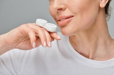 cropped view of cheerful woman holding contact lenses and smiling happily on gray backdrop clipart