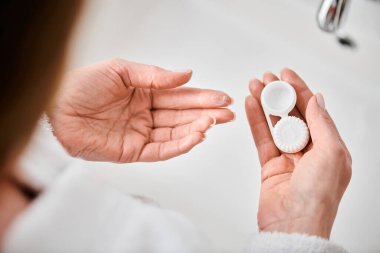 cropped view of adult woman in bathrobe holding her contact lenses before wearing them in bathroom clipart