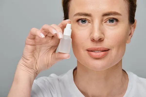 stock image cheerful good looking woman holding eye drops and looking straight at camera on gray backdrop