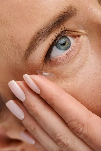 stock image close up of attractive female model wearing her contact lens while posing on gray background