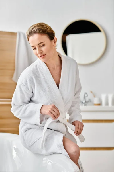 stock image good looking jolly woman with blonde hair in white cozy bathrobe posing next to her bathtub