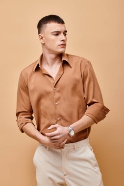 Portrait of stylish handsome man in beige shirt looking away on peachy beige background clipart