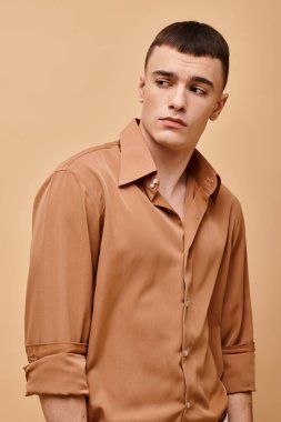 Bej gömlekli şık yakışıklı bir adamın moda portresi şeftali rengi arka planda başka tarafa bakıyor.