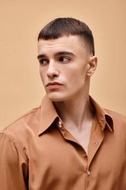 Bej gömlekli şık yakışıklı bir adamın moda portresi şeftali rengi arka planda başka tarafa bakıyor.