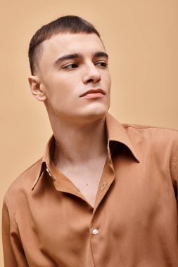 Fashion portrait of stylish young man in beige shirt looking away on peachy beige background clipart