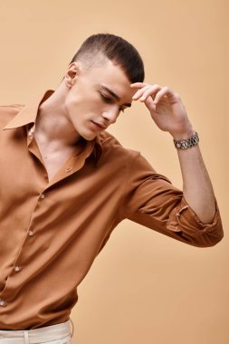 Portrait of young handsome man in beige shirt looking down on peachy beige background clipart