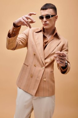 Bej ceketli şık yakışıklı adamın portresi şeftali rengi arka planda ellerini hareket ettiriyor.