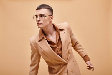 20 'li yaşlarda şık bej ceketli ve şeftali rengi arka planda gözlüklü şık bir adam.