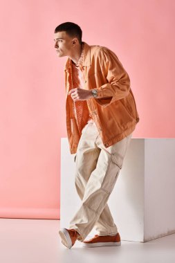 Bej gömlekli şık bir adamın tam boy resmi, pembe arka planda beyaz küplü pantolonlar ve botlar.