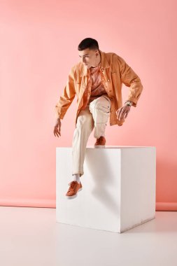Pembe arka planda beyaz küpten atlayan bej renkli kıyafetli şık bir adamın moda portresi.