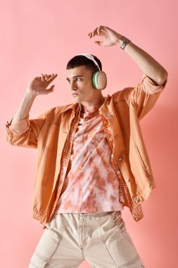 Kablosuz kulaklıklı, katmanlı bir adam pembe arka planda müzik eşliğinde dans ediyor.