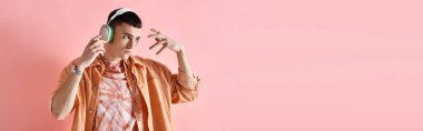 Kablosuz kulaklıklı, pembe arka planda müzik eşliğinde dans eden katmanlı bir adamın portresi.