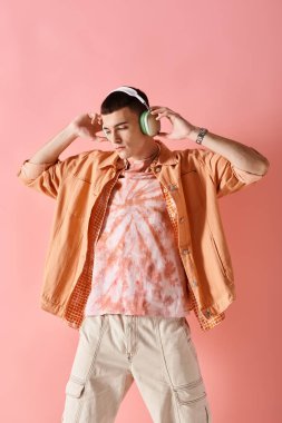 Stylish man in layered outfit with wireless headphones dancing to music on pink background clipart