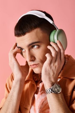 Pembe arka planda müzik dinleyen kablosuz kulaklıklı bir adam portresi.