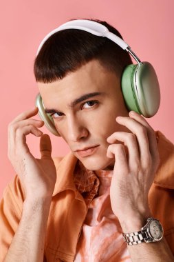 Kablosuz kulaklıklı yakışıklı adam pembe arka planda müzik dinliyor ve kameraya bakıyor.