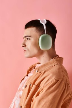 Modayı izleyen, kablosuz kulaklık takan, pembe arka planda müzik dinleyen bir adam.