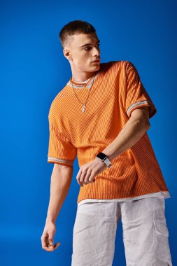 Turuncu gömlekli ve mavi arka planda beyaz şortlu yakışıklı bir adamın moda portresi.