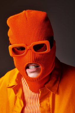 Turuncu elbiseli cesur adamın portresi kar maskesi ve kahverengi arka planda turuncu güneş gözlüğü takıyor.