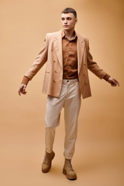 Full length portrait of fashionable man in beige jacket, shirt, pants and boots on beige background clipart