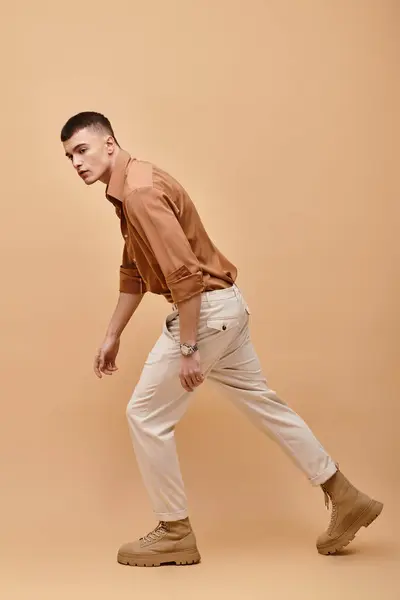 stock image Side view image of stylish man in beige jacket, shirt, pants and boots posing on beige background