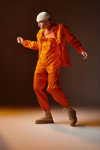 Stylowy Mężczyzna Pomarańczowym Kombinezonie Kurtce Beżowa Czapka Pozująca Brązowym Tle — Zdjęcie stockowe