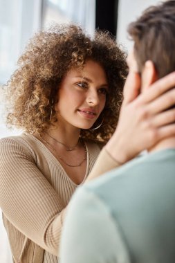 Beautiful young woman in love at looking at boyfriend, smiling happily and touching his cheek clipart