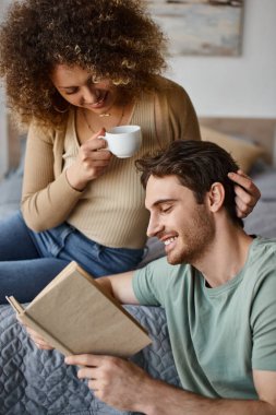 curly young woman and brunette man engage in lively talk over coffee, book in his hands clipart