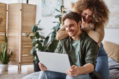 Dizüstü bilgisayarlarıyla birlikte oturan kıvırcık saçlı genç kadın ve esmer adam huzurlu bir sabahın tadını çıkarıyor.